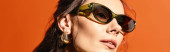 A stylish woman wearing round sunglasses against an orange background exuding summertime fashion vibes. puzzle #711222776