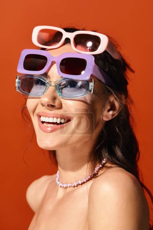 A fashionable woman in sunglasses and a necklace posing against an orange background in a studio setting.