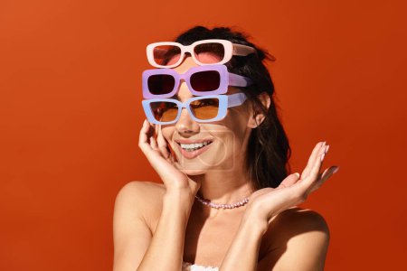A stylish woman with sunglasses strikes a pose in a studio against an orange background.