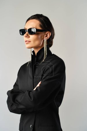 Confident woman exuding elegance in black attire and shades against a neutral backdrop.