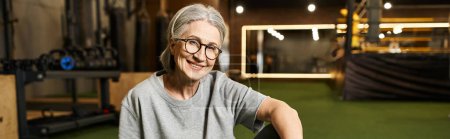 Photo for Positive mature woman with glasses and gray hair sitting on floor and smiling at camera, banner - Royalty Free Image