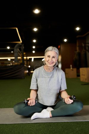 Photo for Joyous mature woman with gray hair in sportswear exercising with dumbbells and looking at camera - Royalty Free Image