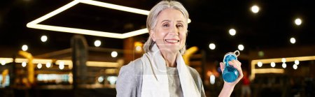 Photo for Senior merry woman with towel and bottle smiling at camera while relaxing after training, banner - Royalty Free Image
