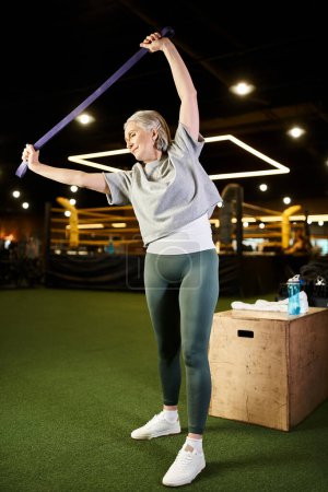 positive senior sportswoman in comfy attire training actively with fitness expander while in gym