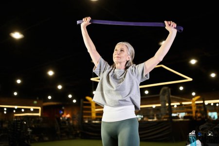 Photo for Smiling senior beautiful sportswoman in comfy attire training with fitness expander while in gym - Royalty Free Image