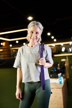 Foto de Alegre mujer mayor en ropa deportiva posando activamente con expansor de fitness y sonriendo a la cámara - Imagen libre de derechos