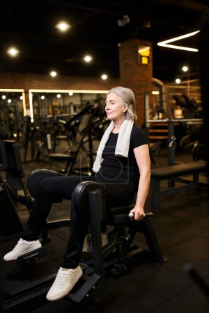 Foto de Mujer mayor alegre y atractiva en entrenamiento de ropa deportiva activamente en la máquina de becerro mientras está en el gimnasio - Imagen libre de derechos