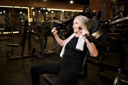 Foto de Mujer de pelo gris madura de buen aspecto en entrenamiento de ropa deportiva activamente en la máquina de prensa de pecho - Imagen libre de derechos