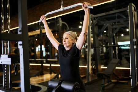 Photo for Appealing mature sportswoman in cozy attire with towel training on lats pulldown machine actively - Royalty Free Image