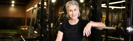 Foto de Alegre atractiva mujer mayor con el pelo gris en ropa deportiva posando y sonriendo a la cámara, pancarta - Imagen libre de derechos