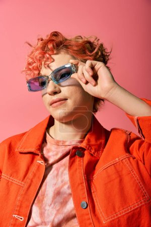 A young woman with vibrant red hair confidently sports sunglasses.