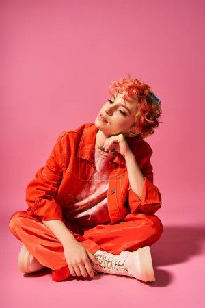 A vibrant woman with red hair sits gracefully on the ground.