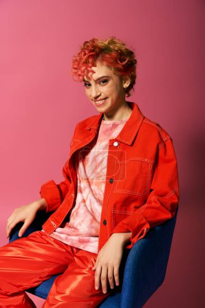 Une jeune femme aux cheveux roux assise sur une chaise bleue.