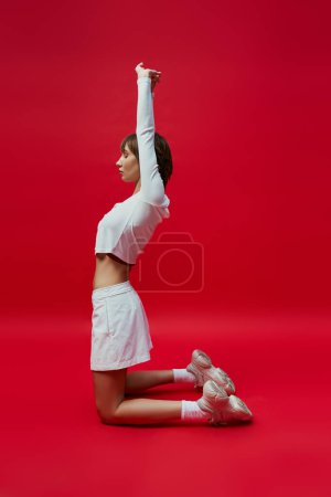 Elegante Frau in weißer Kleidung, die anmutig Yoga vor leuchtend rotem Hintergrund macht.