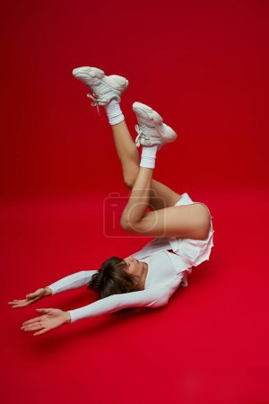 A stylish woman in a white suit and tennis shoes strikes a pose on a vibrant red backdrop.