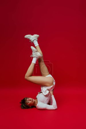 Foto de Young woman in white sportswear performs yoga on vibrant red background. - Imagen libre de derechos