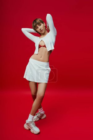 Photo for A stylish woman in a white outfit strikes a pose against a vibrant red backdrop. - Royalty Free Image