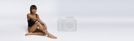 Téléchargez les photos : Jeune femme se détend gracieusement en maillot de bain noir sur le sol. - en image libre de droit
