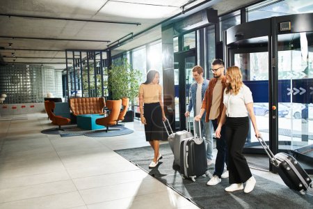 Un grupo multicultural de colegas en atuendo casual navega por un aeropuerto con su equipaje durante un viaje de negocios.