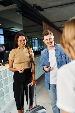 Photo for A man and a women, multicultural colleagues with luggage, stand together in a hotel lobby during a corporate trip. - Royalty Free Image