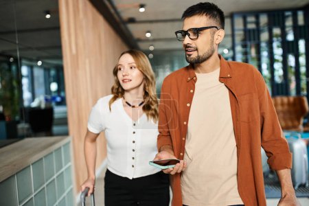 Un homme et une femme en tenue décontractée, se promenant dans un couloir d'hôtel lors d'un voyage d'affaires.