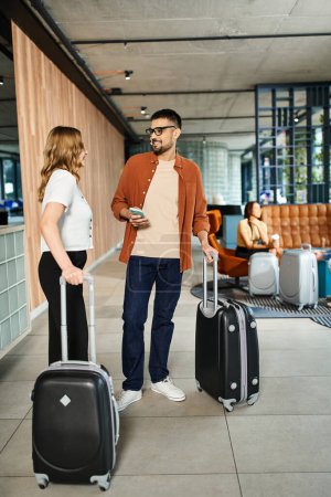 A man and woman stand in an hotel with luggage, ready for their corporate trip as businesspeople in casual clothes.
