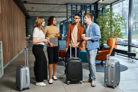 Multicultural group of businesspeople in casual attire standing around with luggage in a hotel lobby during a corporate trip.