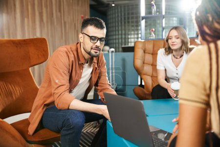 Diverso grupo de empresarios con atuendo casual sentados alrededor de una mesa con ordenadores portátiles en el vestíbulo de un hotel.