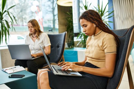 Eine Frau sitzt auf einem Stuhl, konzentriert auf ihren Laptop und beschäftigt sich mit modernen geschäftlichen Aufgaben in einem Coworking Space.