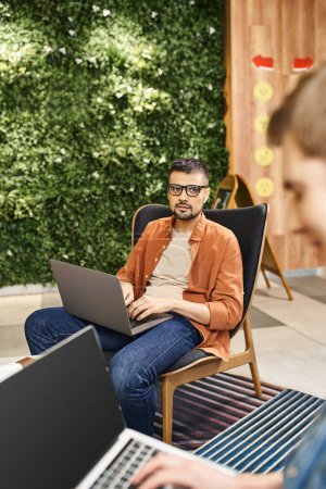 Ein hochkonzentrierter Mann sitzt auf einem Stuhl und tippt während einer Coworking-Session auf einem Laptop