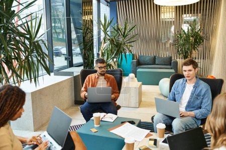 Un groupe diversifié de collègues assis autour d'une table avec des ordinateurs portables, collaborant sur des projets dans un espace de coworking moderne.