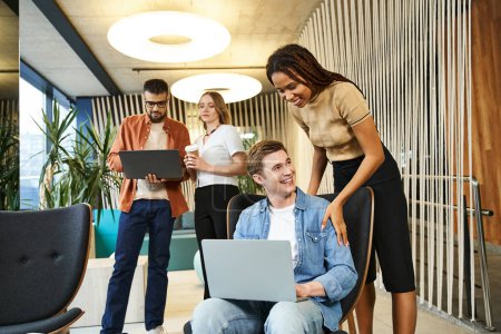 Une équipe de collègues entoure un homme sur un ordinateur portable, collaborant à un projet dans un espace de coworking moderne.