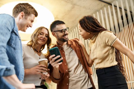 Foto de Un grupo de colegas en un espacio de coworking, reunidos alrededor de una pantalla de smartphone, comprometidos en la colaboración digital. - Imagen libre de derechos