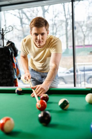 A man from a coworking startup team is playing pool in a room, taking a break from the modern business lifestyle.