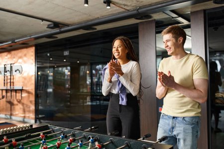 Un hombre y una mujer de un equipo de startups diseñan estrategias alrededor de una mesa de futbolín en un moderno espacio de coworking.