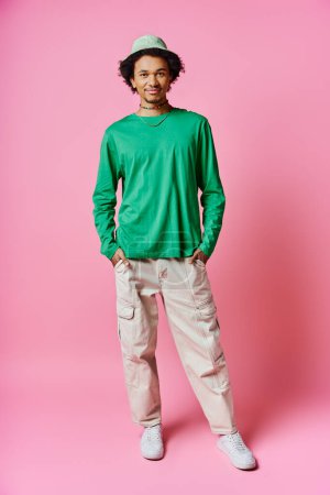 A cheerful young African American man with curly hair wearing casual green shirt and khaki pants against a pink background.