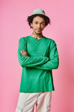 Foto de Un joven y alegre afroamericano con el pelo rizado usando una camisa verde y pantalones sobre un fondo rosa. - Imagen libre de derechos