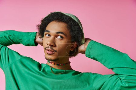 Photo for A young African American man with curly hair in a green shirt looking away, holding his head in his hands. - Royalty Free Image