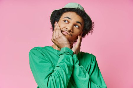 Foto de Un joven afroamericano pensativo con una camisa verde posa sobre un fondo rosa. - Imagen libre de derechos