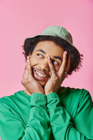 Ein fröhlicher junger afroamerikanischer Mann mit lockigem Haar und grünem Hemd auf rosa Hintergrund.