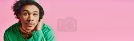 Verblüffter junger afroamerikanischer Mann mit lockigem Haar, lässig gekleidet und mit überraschendem Gesichtsausdruck auf rosa Hintergrund.