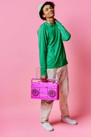 Cheerful African American man in green shirt holding pink radio on pink background, displaying emotions.