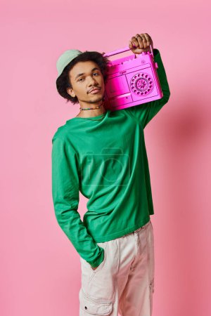 A cheerful young African American man in a green shirt holding a pink boombox on a pink background.