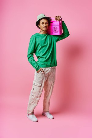 A cheerful young African American man in a green shirt holds a pink boombox, showcasing emotion on a pink background.