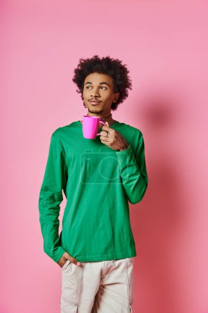 Cheerful African American man in green shirt holds a pink cup against a vibrant pink background.