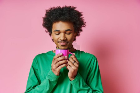 Fröhlicher afroamerikanischer Mann mit lockigem Haar im grünen Hemd, der eine rosa Tasse in der Hand hält und Emotionen ausdrückt.