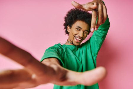 A joyful African American man, curly hair in a green shirt, dances energetically on a vibrant pink background.