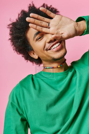 Photo for A cheerful young African American man in a green shirt, holding his hand up to his face, showcasing an emotional gesture. - Royalty Free Image
