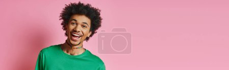 A cheerful young African American man with curly hair, wearing casual green shirt, smiling on pink background.