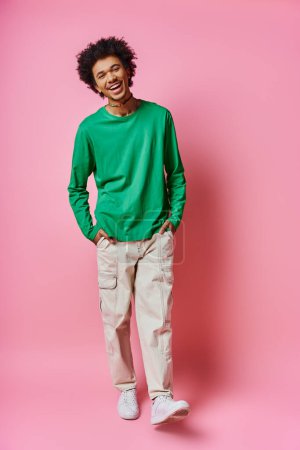 A cheerful young curly Afro-American man stands in casual wear, displaying a range of emotions against a pink background.